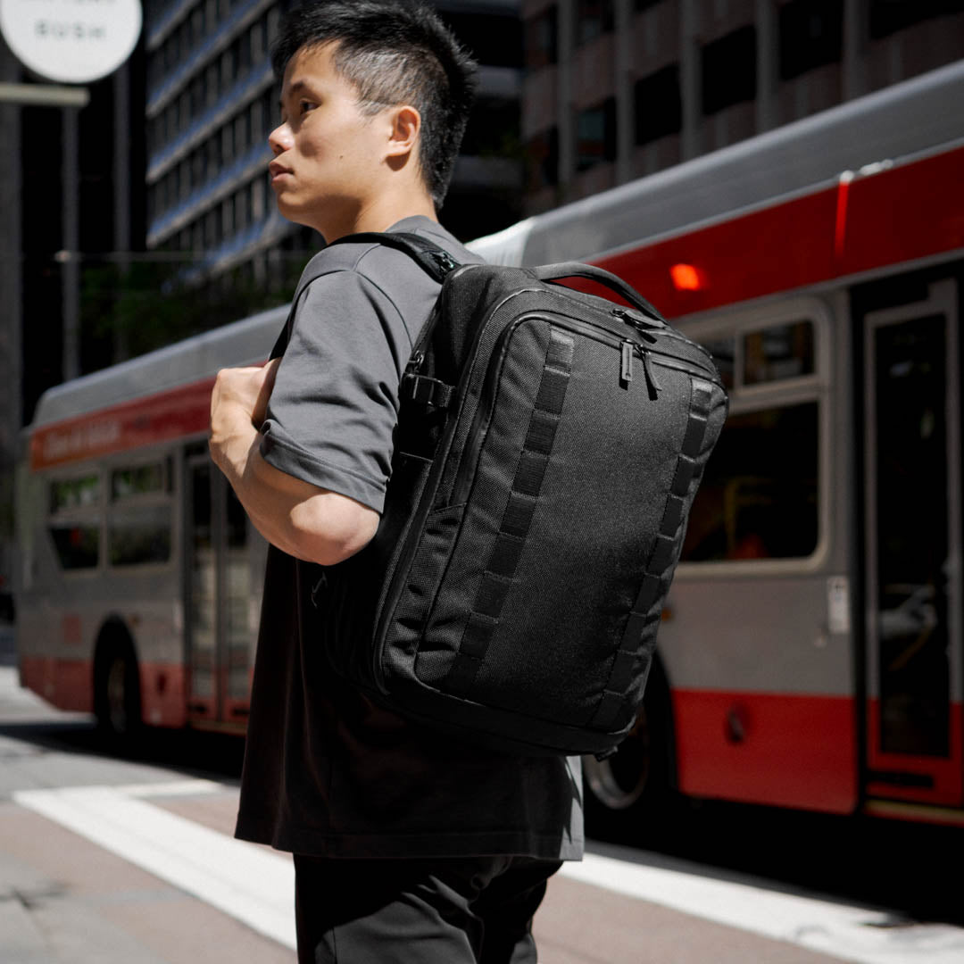 Back view of model carrying the 22L Reset Pack by Rework Gear in front of a red bus.