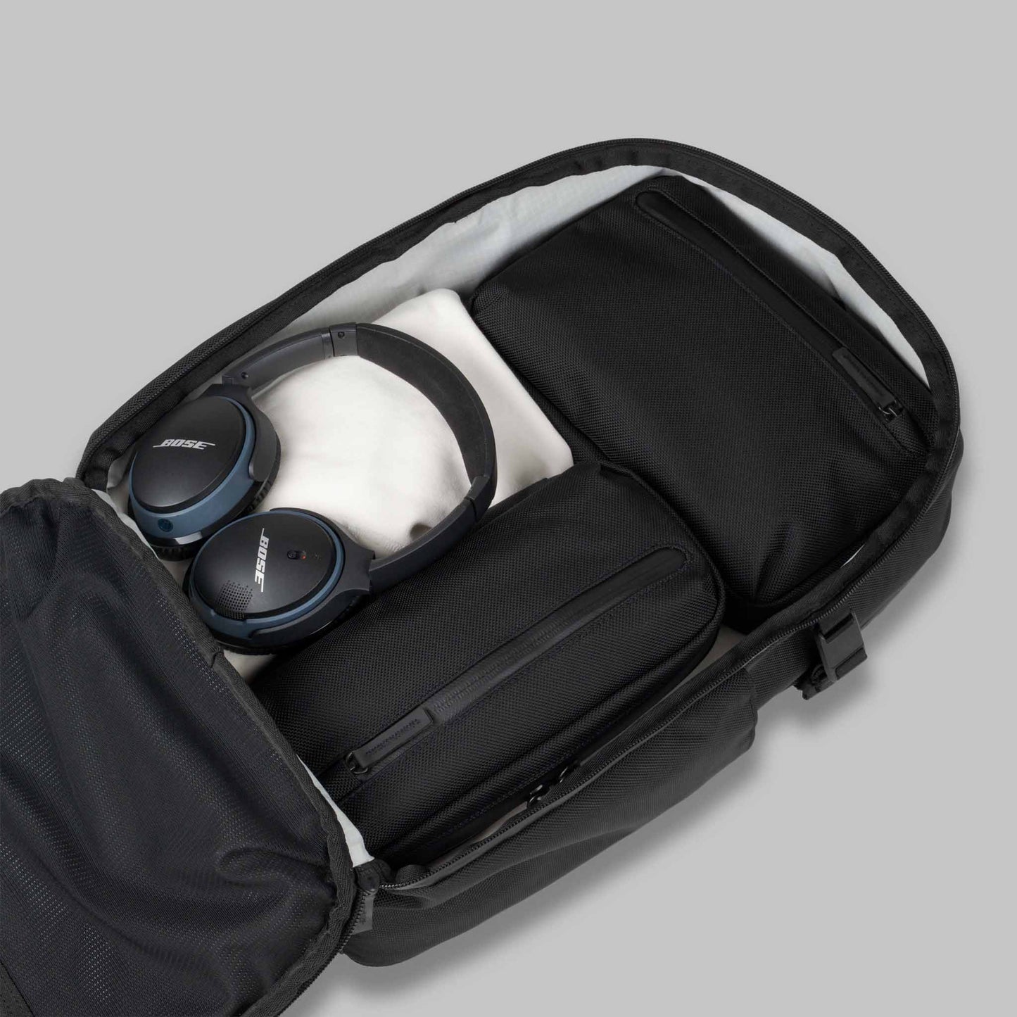 Open main compartment of the 22L Reset Pack by Rework Gear packed with pouches and headphones against a gray background.