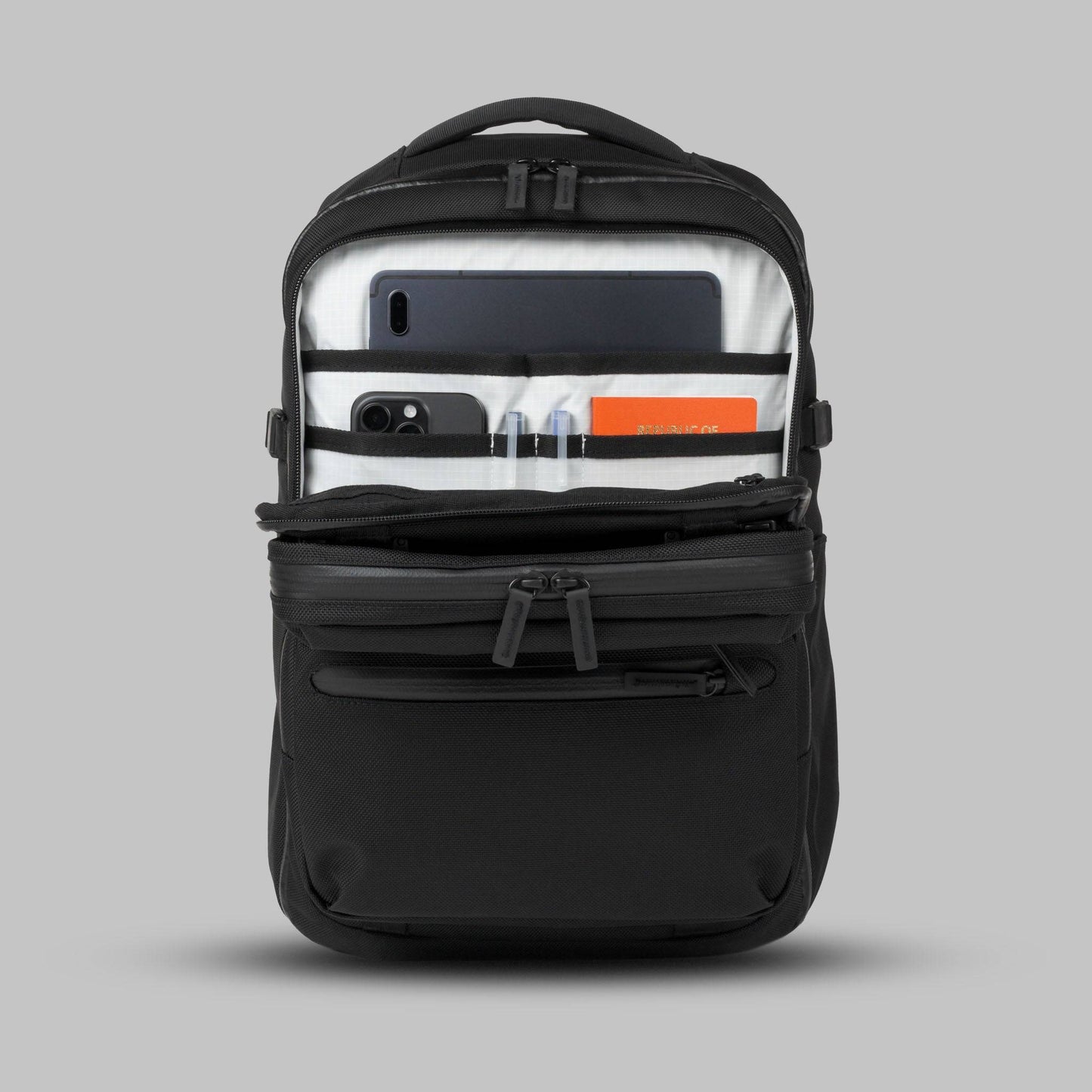 Open front admin compartment of a modular backpack called Reset System packed with essential items against a gray background.