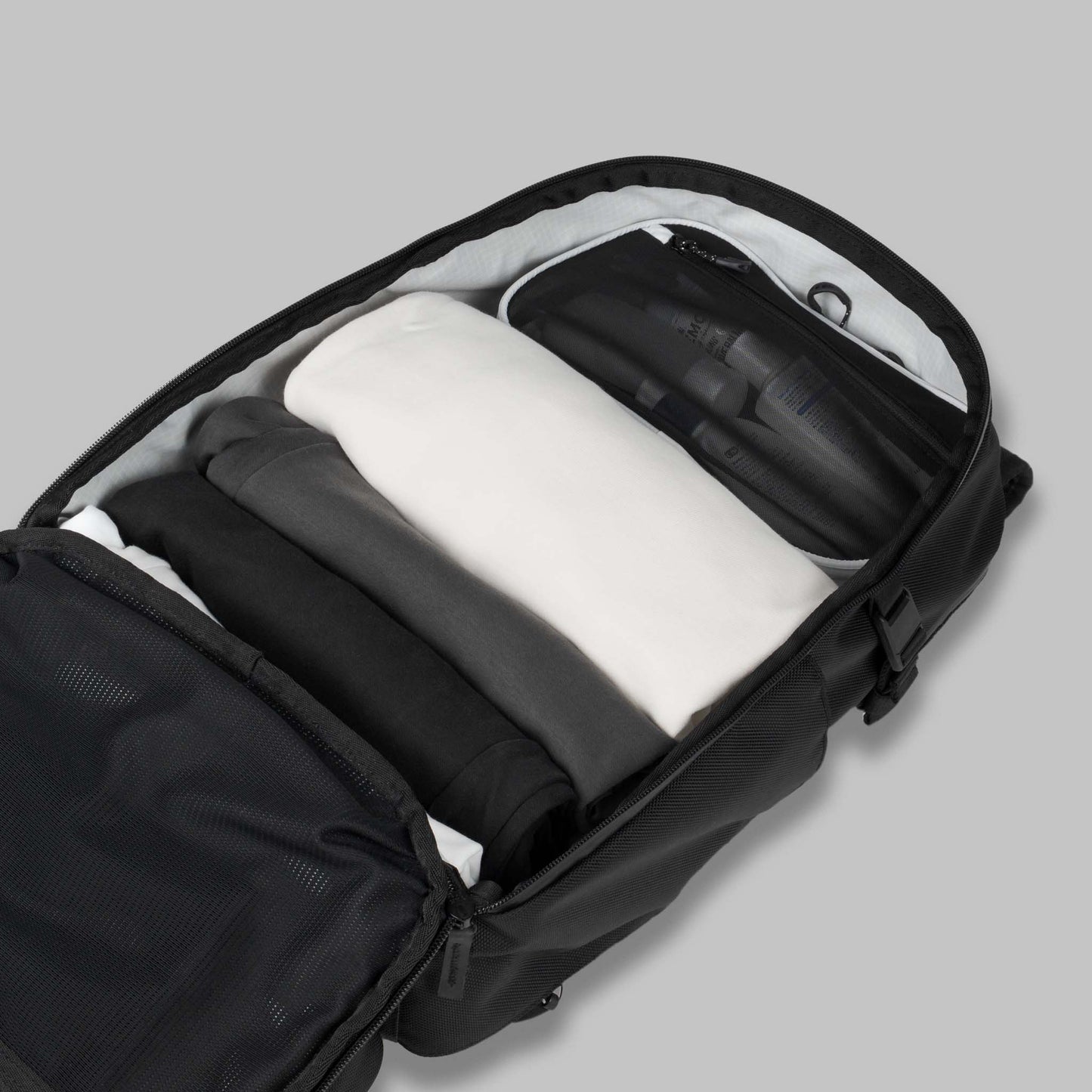 Open main compartment of a modular backpack called Reset System packed with clothing against a gray background.