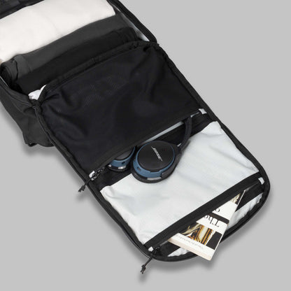 Main compartment zipped pockets of a modular backpack called Reset System packed with a book and headphones against a gray background.